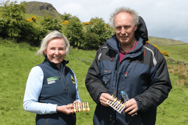 Two people holding tags with a view of the countryside behind them
